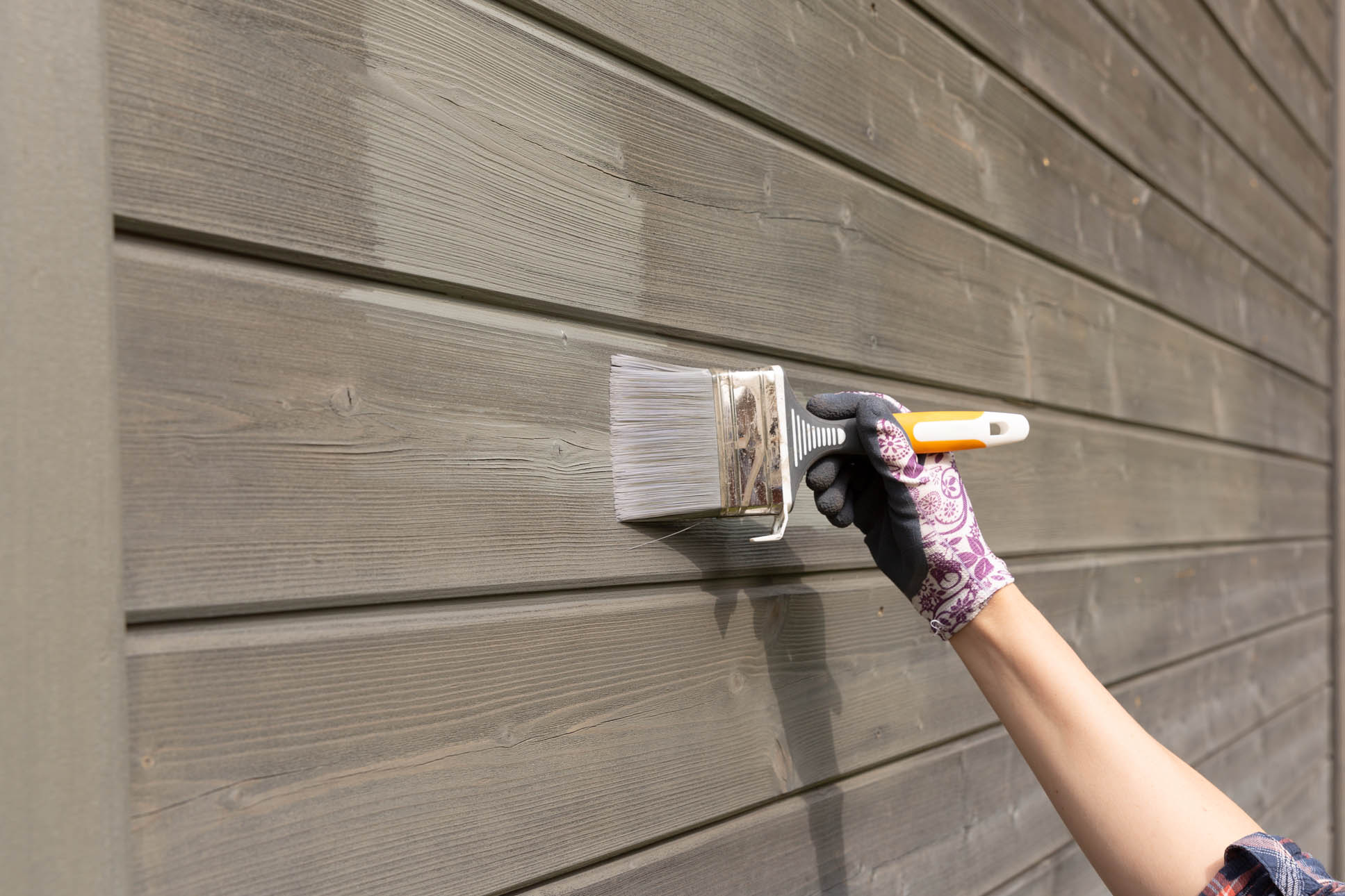 Woman worker painting wooden house exterior wall with paintbrush
