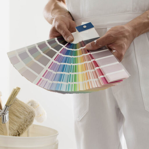 hands of house painter man decorator choose the color using the sample swatch, work of the house to renovate, a wooden ladder with paint brushes and a bucket as a background, close up